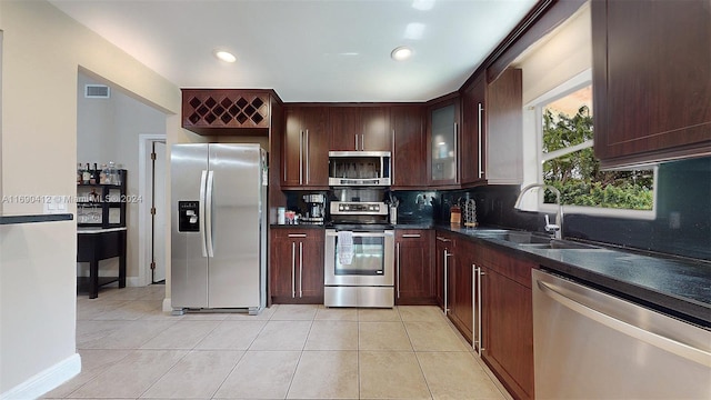 kitchen with stainless steel appliances, dark brown cabinetry, light tile patterned floors, decorative backsplash, and sink