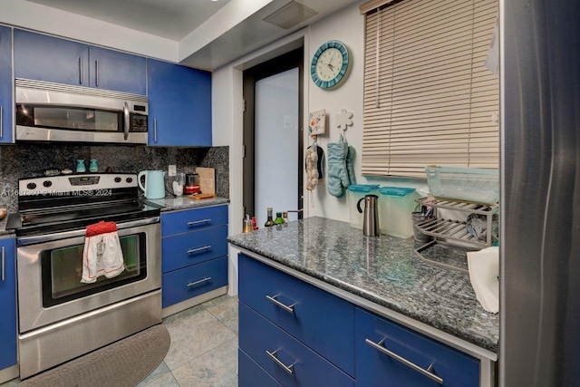 kitchen featuring stainless steel appliances, tasteful backsplash, dark stone countertops, light tile patterned floors, and blue cabinets