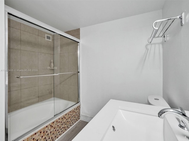 bathroom with hardwood / wood-style floors, combined bath / shower with glass door, and toilet