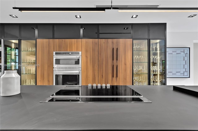 kitchen featuring brown cabinets, glass insert cabinets, stainless steel double oven, modern cabinets, and black electric cooktop