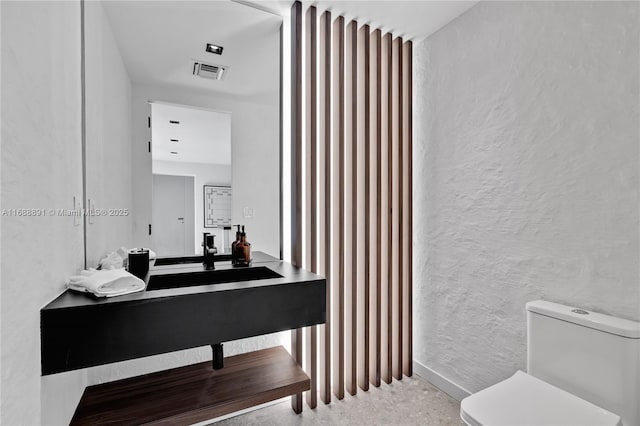 half bath with visible vents, a textured wall, vanity, and toilet