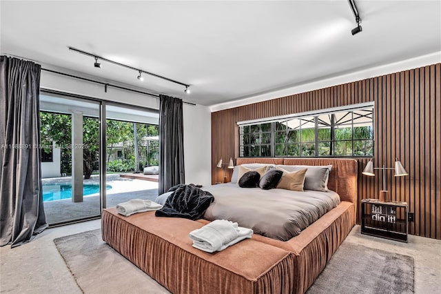 bedroom featuring concrete floors, access to outside, wooden walls, and track lighting