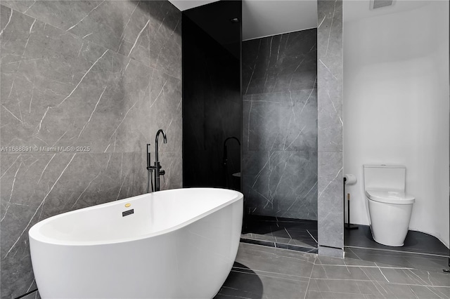 bathroom featuring a freestanding bath, walk in shower, toilet, and tile walls