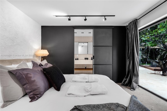 bedroom with rail lighting, ensuite bath, concrete flooring, and a textured wall