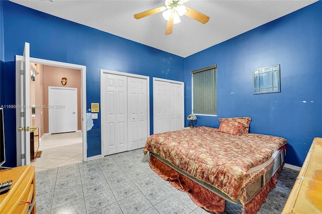 bedroom featuring multiple closets, a textured ceiling, light tile patterned floors, and ceiling fan