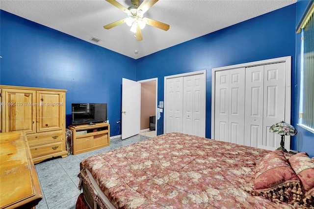 tiled bedroom featuring a textured ceiling, ceiling fan, and two closets