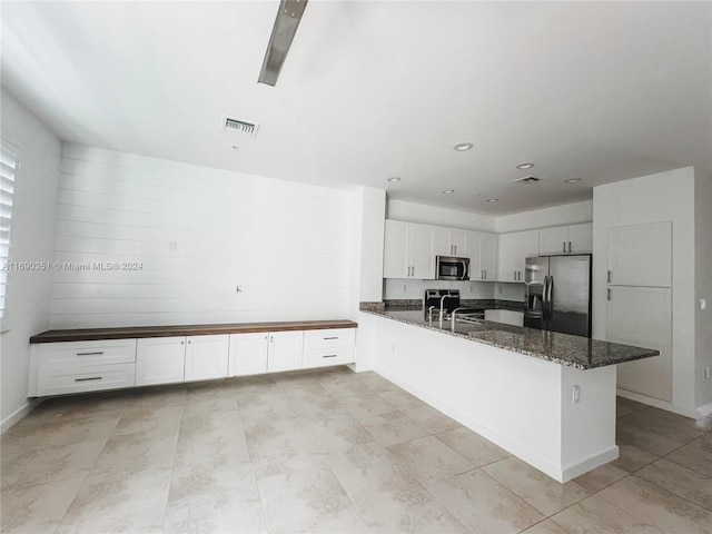 kitchen featuring stainless steel appliances, white cabinetry, dark stone counters, and sink