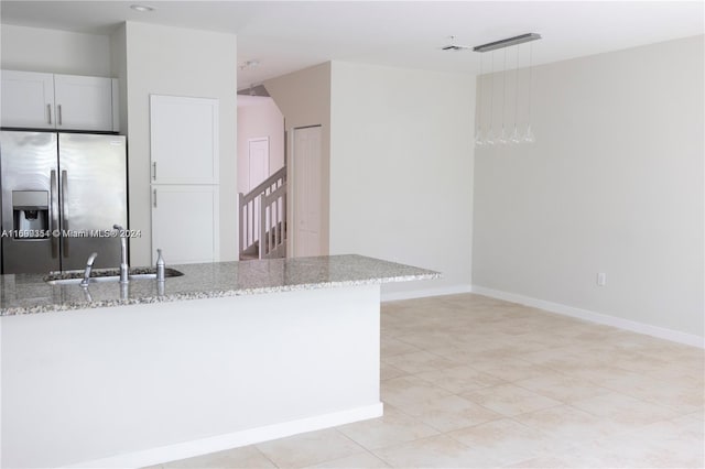 kitchen with stainless steel fridge, light stone counters, sink, decorative light fixtures, and white cabinetry