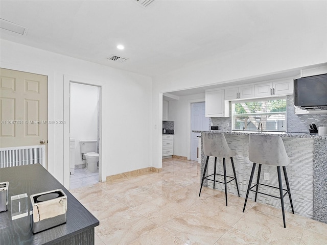 kitchen with white cabinets, a kitchen breakfast bar, dark stone counters, and sink