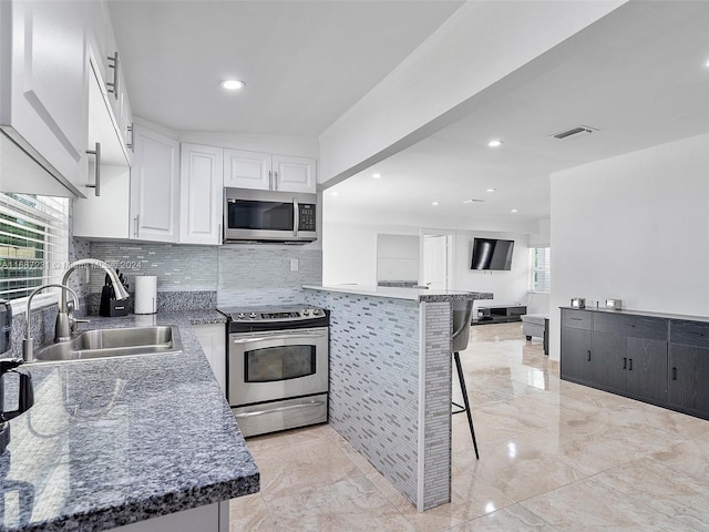 kitchen featuring white cabinets, sink, dark stone countertops, appliances with stainless steel finishes, and a kitchen bar