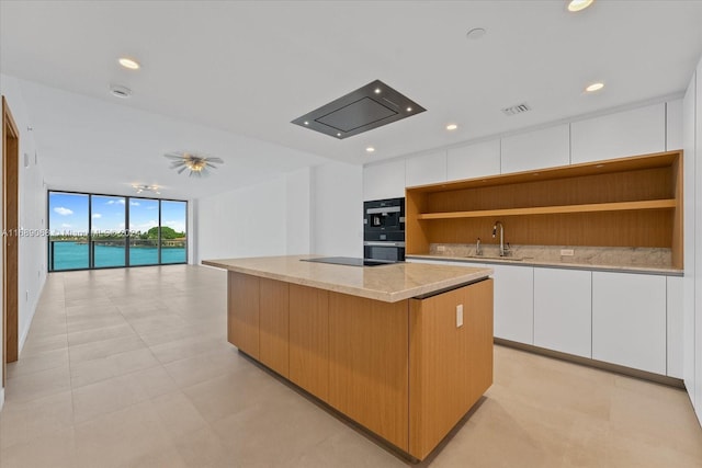 kitchen with sink, a kitchen island, a wall of windows, white cabinets, and a water view