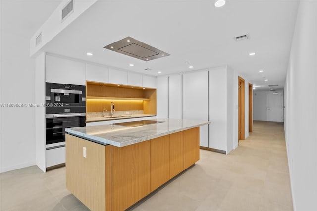 kitchen featuring light stone countertops, white cabinetry, sink, a spacious island, and black electric stovetop