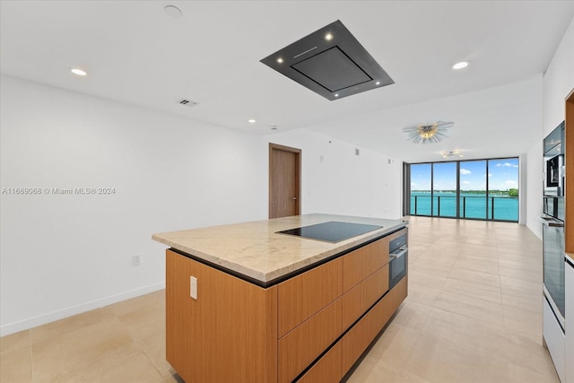 kitchen with floor to ceiling windows, oven, a spacious island, light stone countertops, and black electric cooktop