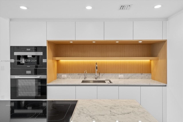 kitchen with white cabinets, double wall oven, sink, light stone countertops, and black electric cooktop