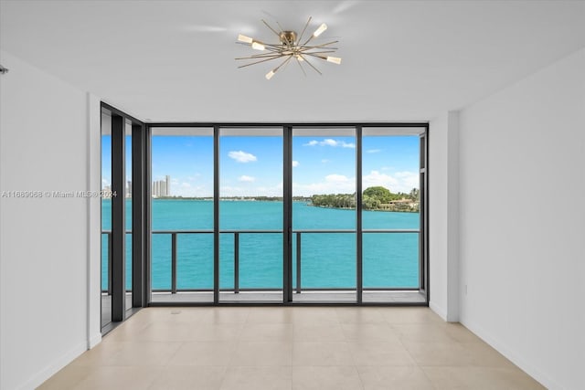 spare room featuring a water view, an inviting chandelier, and expansive windows