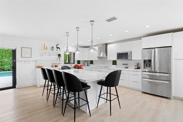 kitchen featuring a kitchen island, appliances with stainless steel finishes, wall chimney exhaust hood, and white cabinets