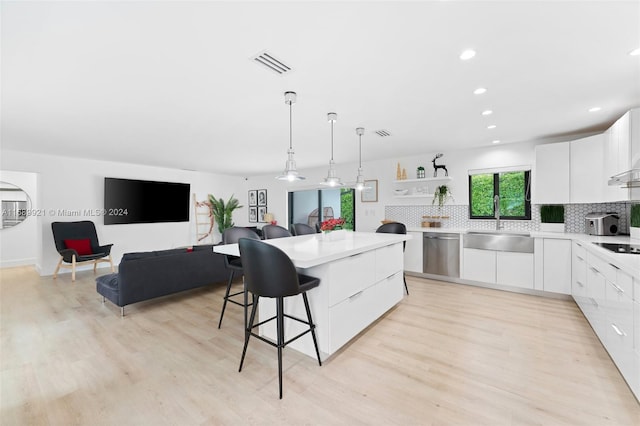 kitchen with sink, stainless steel dishwasher, white cabinetry, light wood-type flooring, and decorative light fixtures