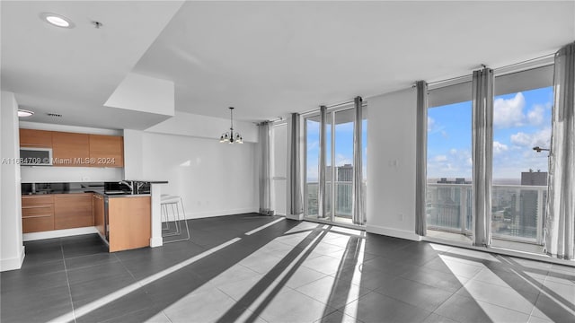 interior space with kitchen peninsula, expansive windows, dark tile patterned flooring, a chandelier, and hanging light fixtures