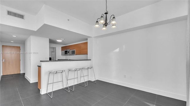 kitchen featuring kitchen peninsula, a kitchen bar, dark tile patterned floors, decorative light fixtures, and an inviting chandelier