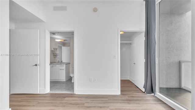 unfurnished bedroom featuring light hardwood / wood-style floors, a spacious closet, sink, and ensuite bath