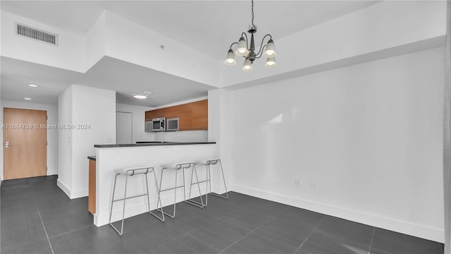 kitchen with kitchen peninsula, a breakfast bar, decorative light fixtures, dark tile patterned flooring, and an inviting chandelier