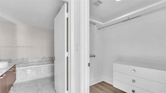 bathroom with wood-type flooring, vanity, and tiled tub