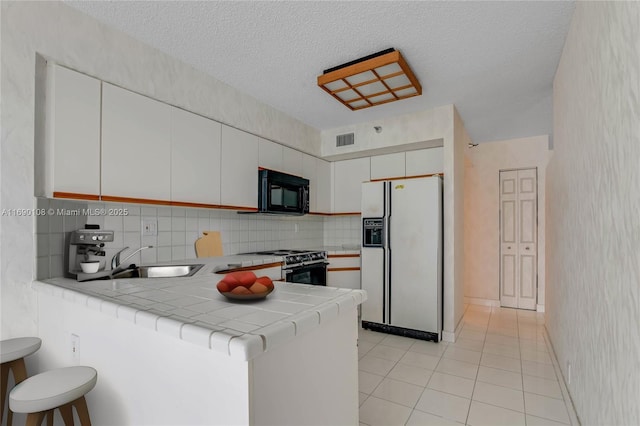 kitchen featuring visible vents, stove, a sink, white fridge with ice dispenser, and black microwave