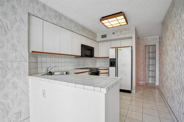 kitchen featuring visible vents, range, a peninsula, white fridge with ice dispenser, and black microwave