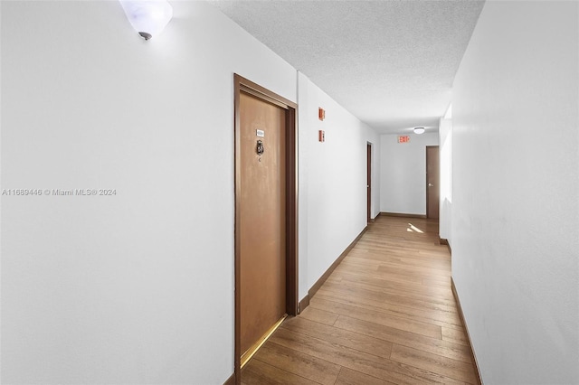 hallway featuring light hardwood / wood-style flooring and a textured ceiling