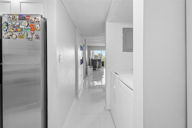 corridor featuring separate washer and dryer, electric panel, light tile patterned flooring, and a textured ceiling