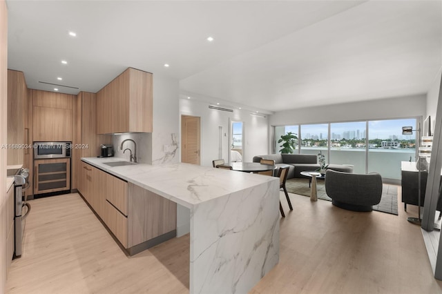 kitchen featuring light hardwood / wood-style floors, a water view, light stone counters, and kitchen peninsula