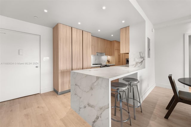 kitchen with light stone counters, stainless steel range oven, tasteful backsplash, a breakfast bar area, and light wood-type flooring