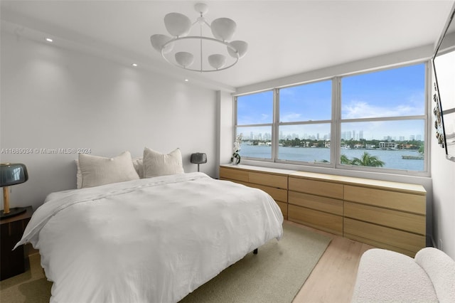 bedroom featuring light hardwood / wood-style floors, a water view, and an inviting chandelier