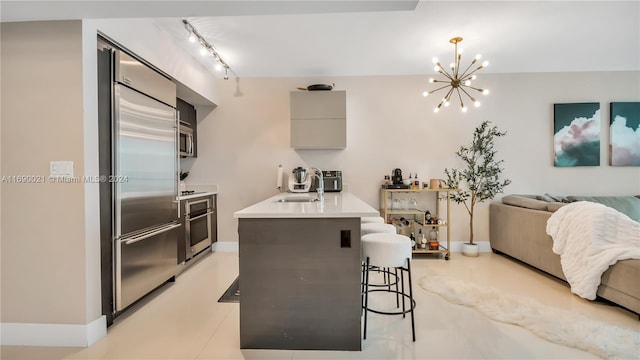 kitchen with a breakfast bar, sink, rail lighting, appliances with stainless steel finishes, and a notable chandelier