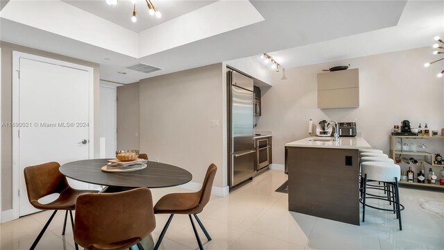 dining room featuring sink, rail lighting, a raised ceiling, a notable chandelier, and light tile patterned flooring