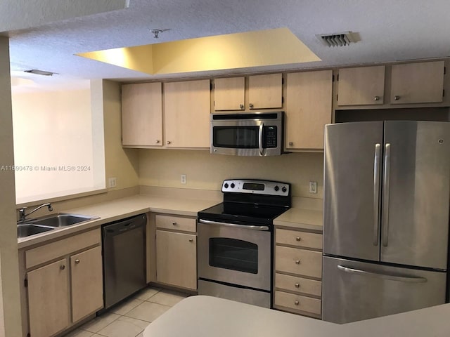 kitchen with a textured ceiling, sink, light tile patterned floors, light brown cabinets, and appliances with stainless steel finishes