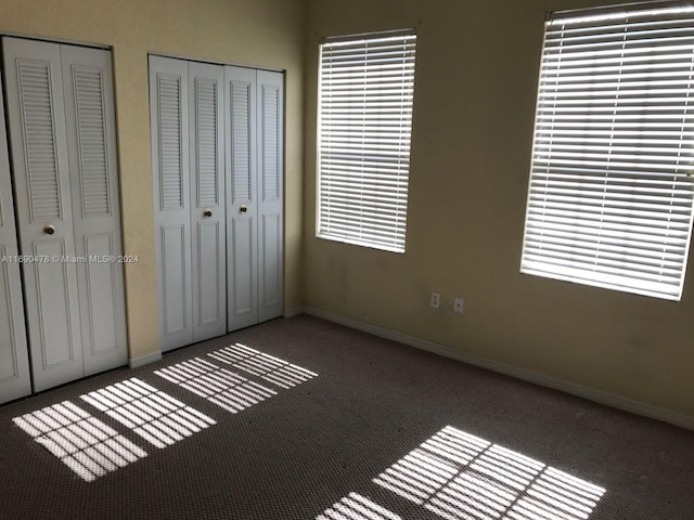 unfurnished bedroom featuring multiple closets and dark carpet