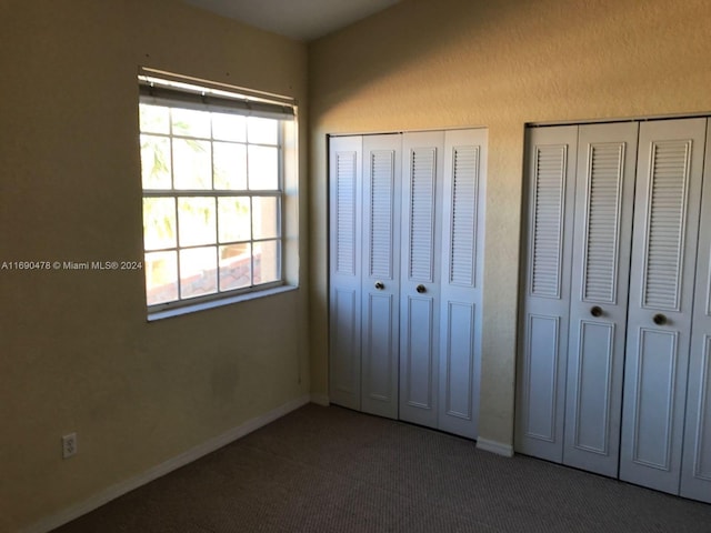 unfurnished bedroom featuring multiple closets and dark colored carpet