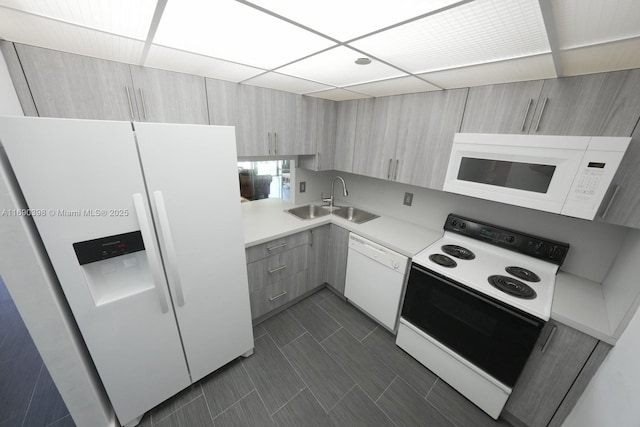 kitchen with light countertops, a sink, modern cabinets, white appliances, and a drop ceiling