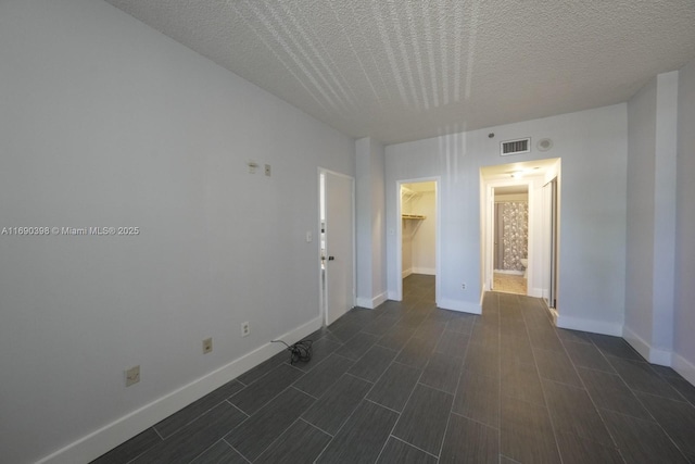 spare room featuring dark wood-type flooring, visible vents, a textured ceiling, and baseboards