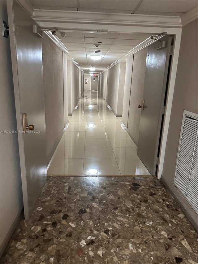 hallway with crown molding, a paneled ceiling, and light tile patterned flooring