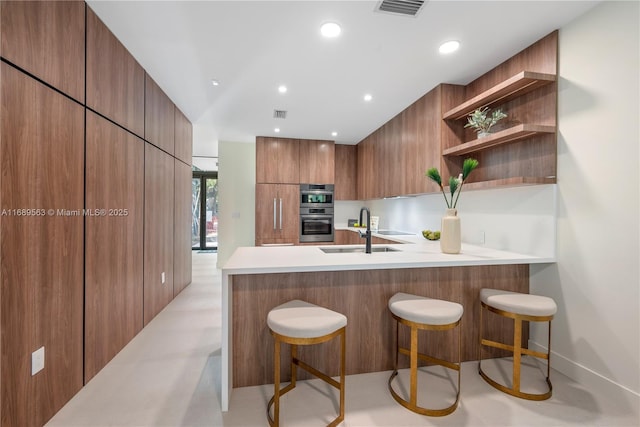 kitchen featuring stainless steel double oven, kitchen peninsula, sink, and a breakfast bar area