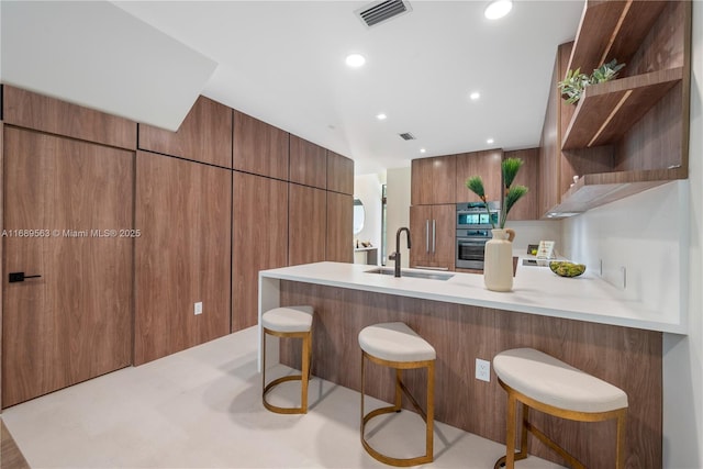 kitchen with modern cabinets, a breakfast bar area, light countertops, stainless steel oven, and open shelves