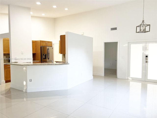 kitchen featuring light tile patterned flooring, a high ceiling, light stone counters, stainless steel fridge with ice dispenser, and pendant lighting