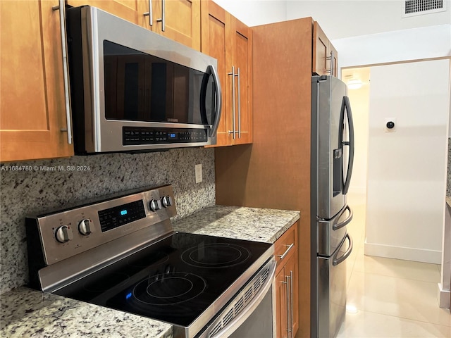 kitchen with tasteful backsplash, light stone countertops, appliances with stainless steel finishes, and light tile patterned flooring