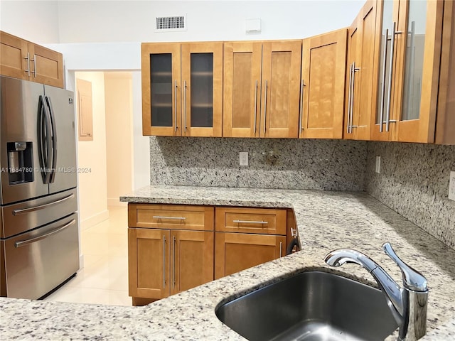 kitchen featuring stainless steel fridge with ice dispenser, sink, light stone counters, and tasteful backsplash