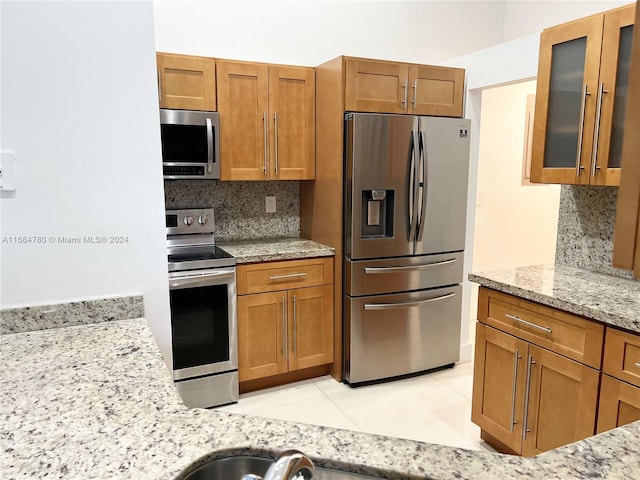 kitchen featuring appliances with stainless steel finishes, light tile patterned flooring, light stone counters, and backsplash