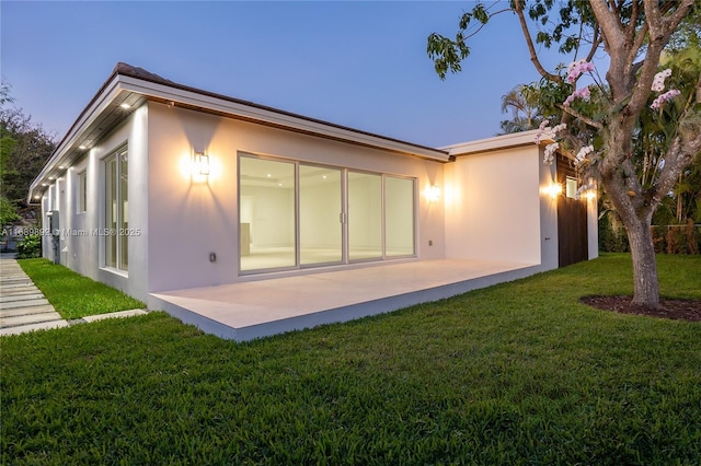 back house at dusk with a lawn and a patio area