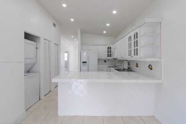 kitchen featuring vaulted ceiling, white cabinets, kitchen peninsula, stacked washer / dryer, and white appliances