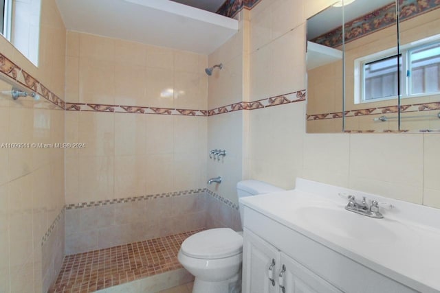 bathroom featuring tile walls, a tile shower, vanity, and toilet